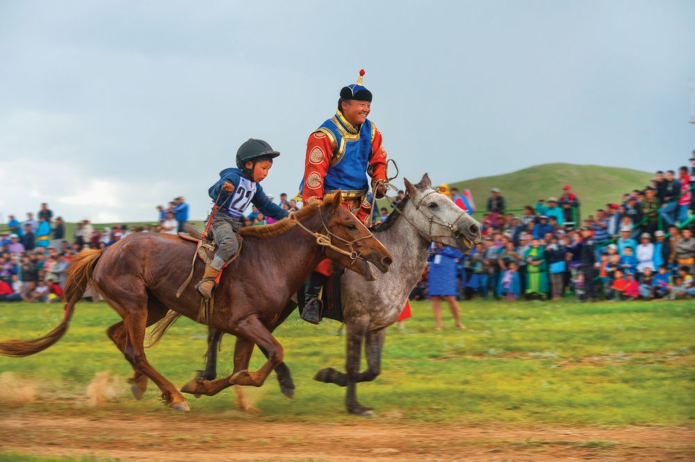 A child and an instructor riding horses in Nadaam festival